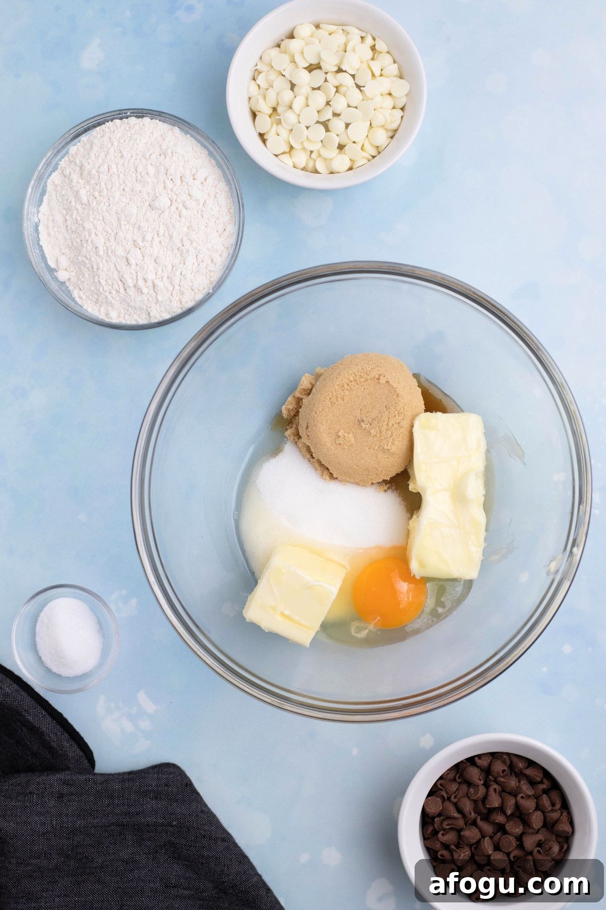 Butter and sugars in a clear glass bowl on a blue table.