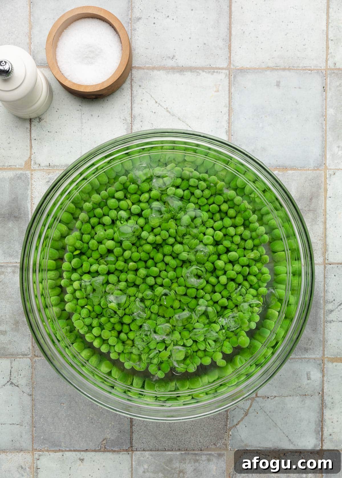 Top-down process photo of peas chilling in an ice water bath to stop the cooking and keep their bright green color.