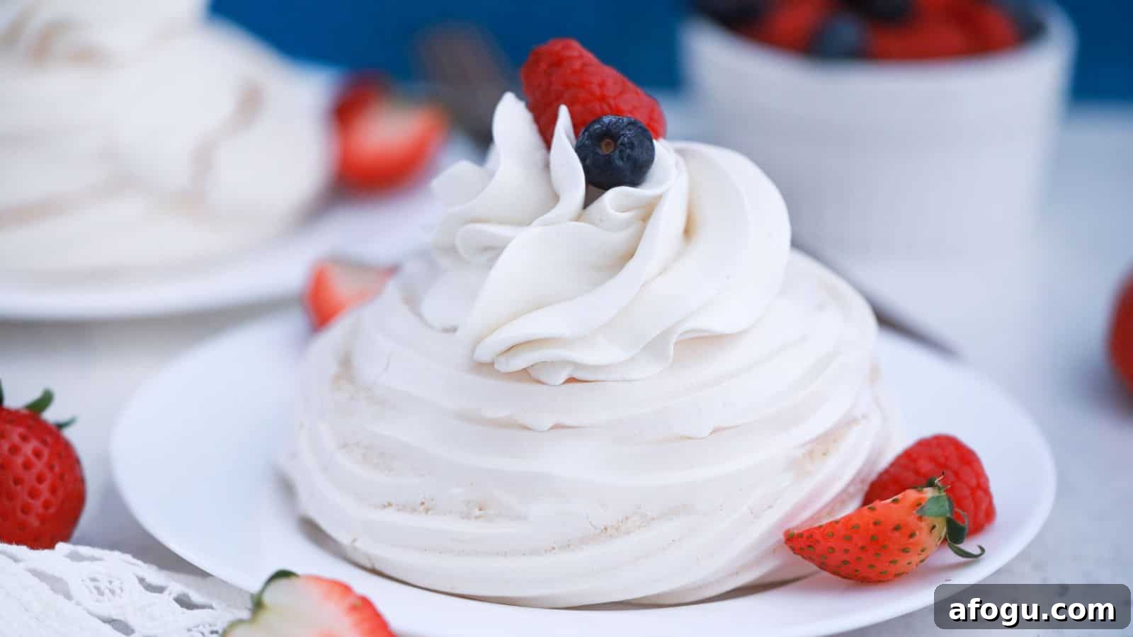 Pavlova dessert with whipped cream and fresh berries on a white plate, garnished with strawberries and blueberries.