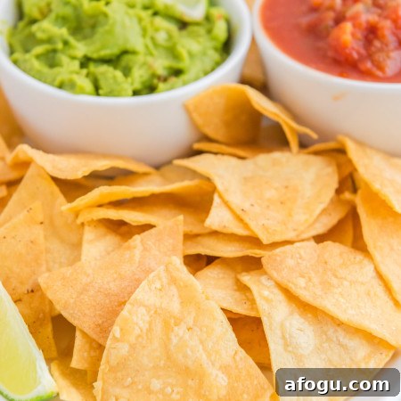Crispy Air Fryer Tortilla Chips Recipe for Homemade Snacking 9 Crispy tortilla chips on a white platter, with 2 dips in the background (guacamole, and salsa)