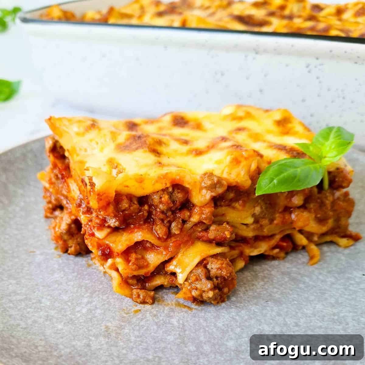 Side view of a slice of lasagna, showing all 4 layers with lots of chunky meaty bolognese in each layer. 
