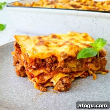 Sideview of a slice of lasagna showing all 4 layers. A tray of lasagna in the background, blurred