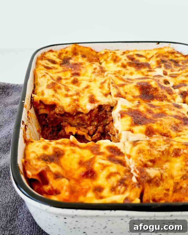 A side view of a tray of lasagna, cut and divided into squares with a piece taken out.