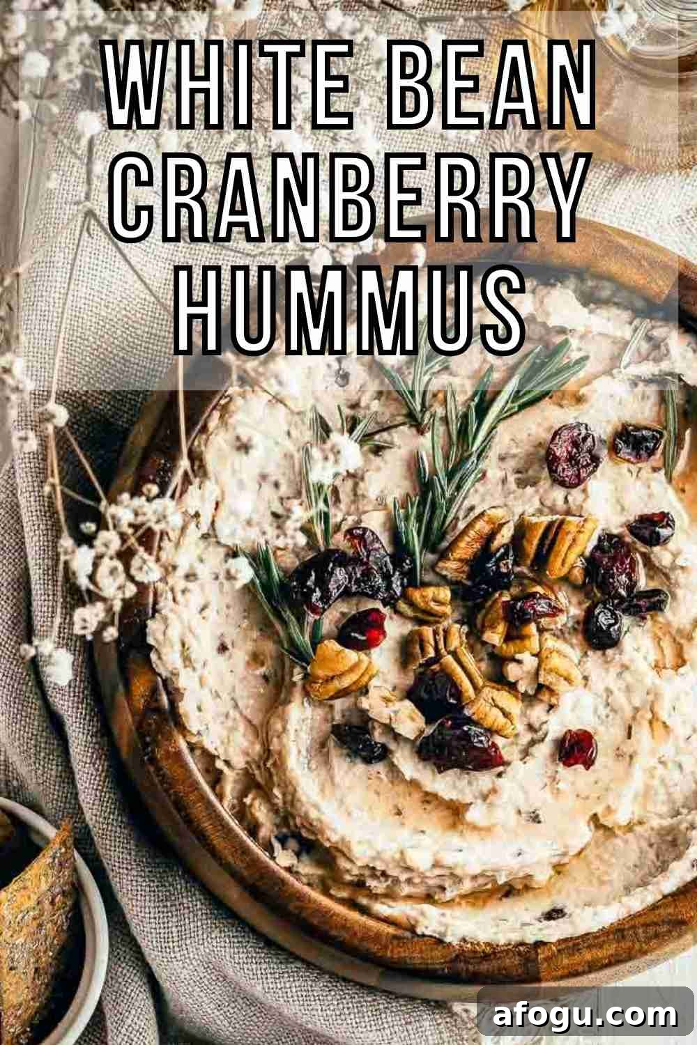 Creamy White Bean and Cranberry Hummus Recipe 2 Overhead shot of hummus garnished with pecans, cranberries, and rosemary in a large wooden bowl on a burlap cloth with rosemary, baby breath, and crackers on the side.