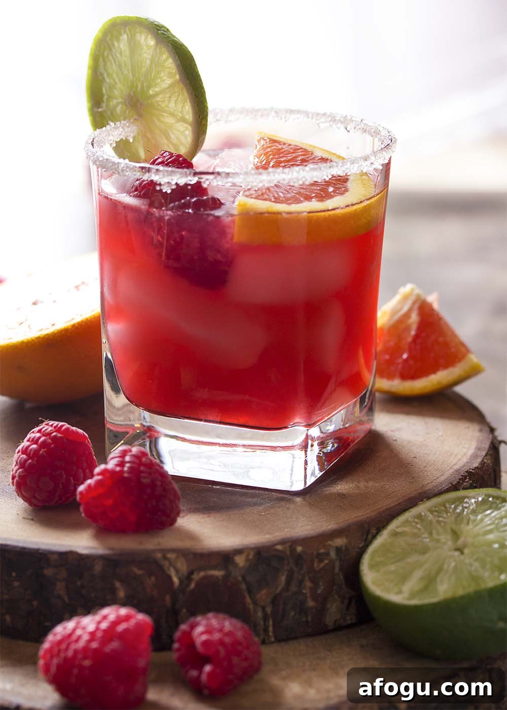 A margarita garnished with lime, orange, and raspberries in a sugar rimmed glass.