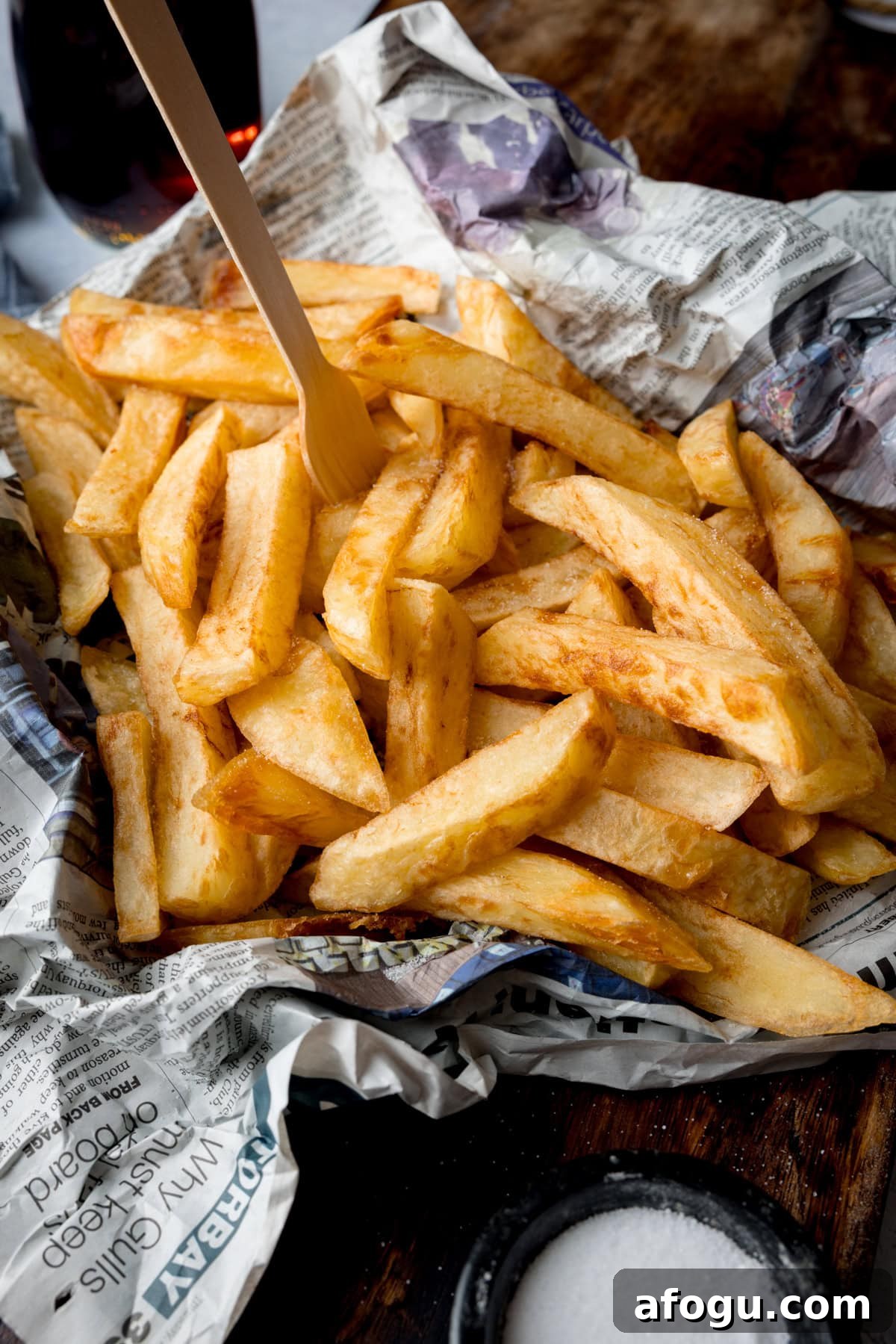 Chip Shop-Style Chips on newspaper with a small wooden fork and a dish of salt.