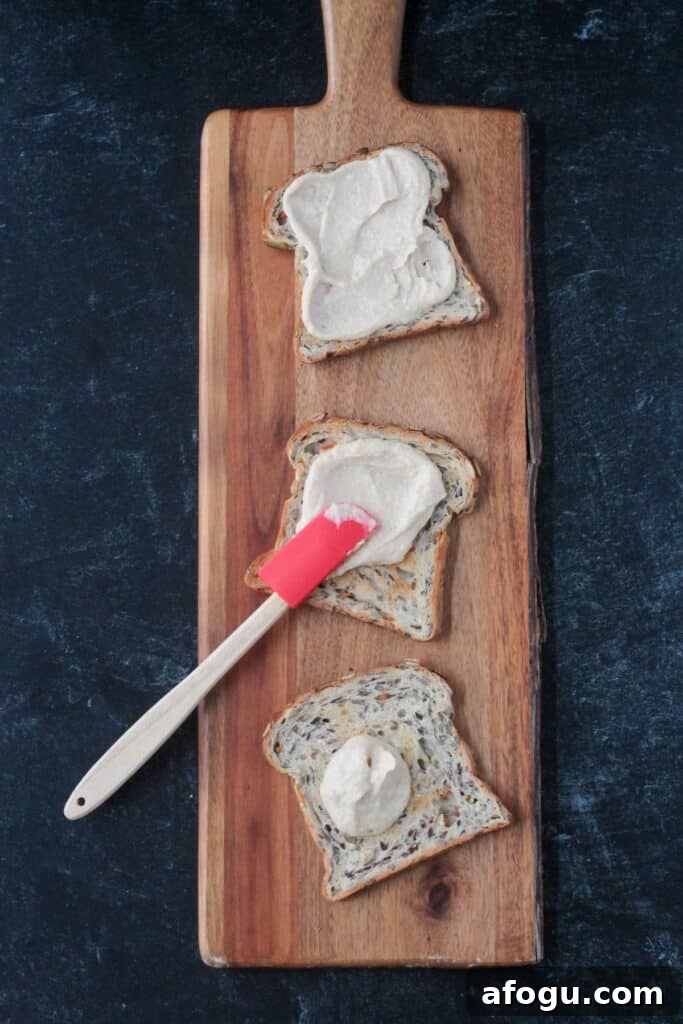 10 Creative Hummus Toast Recipes for Quick Snacks 5 Spreading hummus on toast with a small red spatula.
