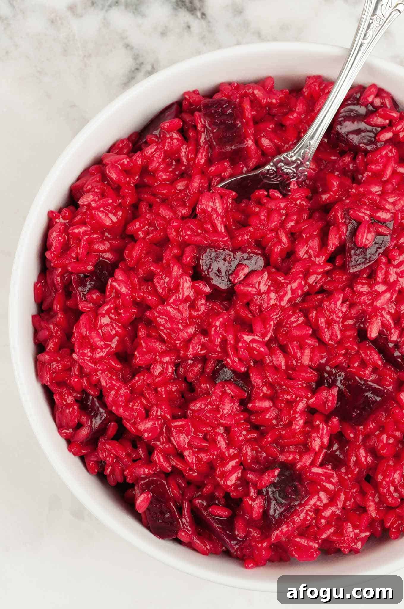 Roasted beet risotto in a white bowl, featuring creamy rice with vibrant red color and chunks of tender beet.