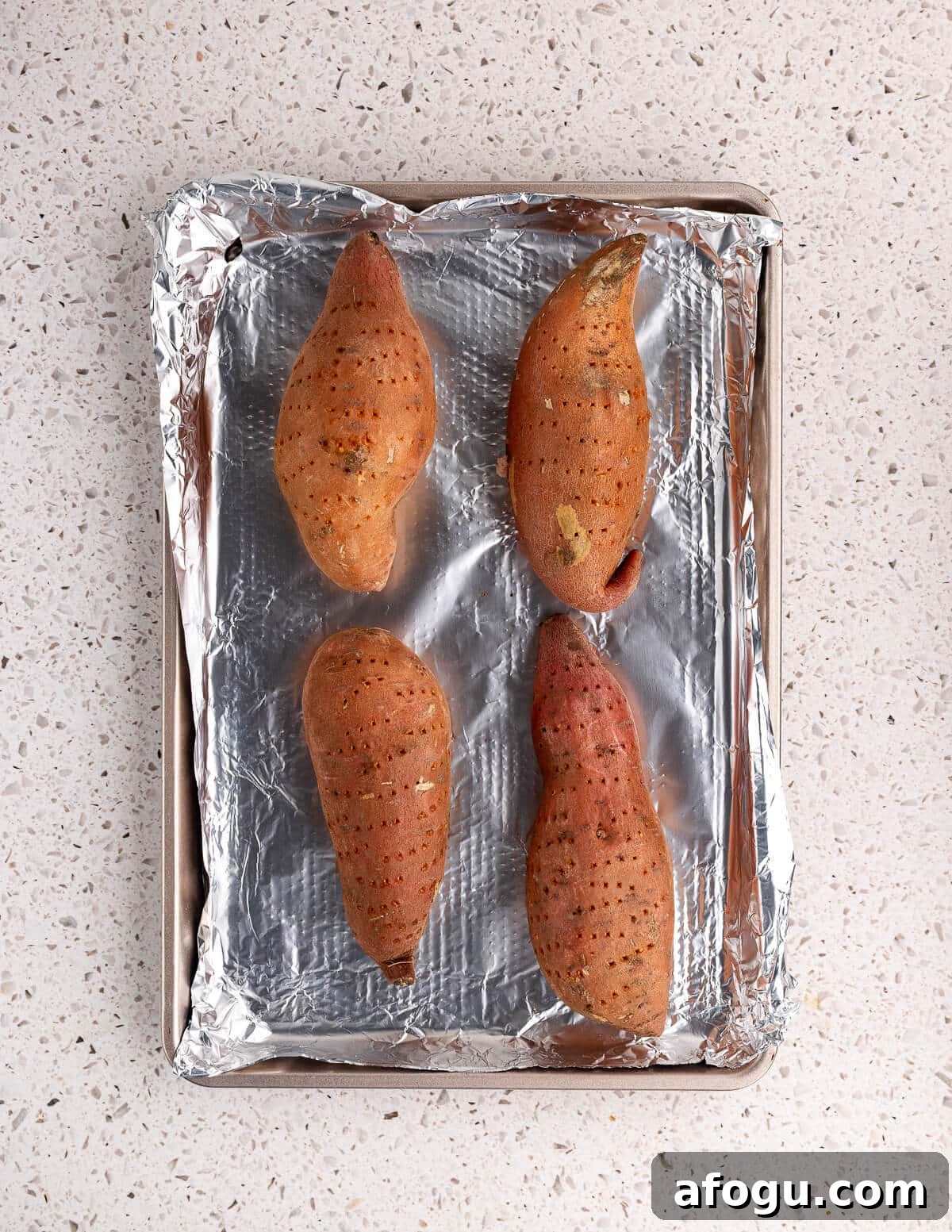 pricked sweet potatoes on an aluminum foil lined sheet pan. 