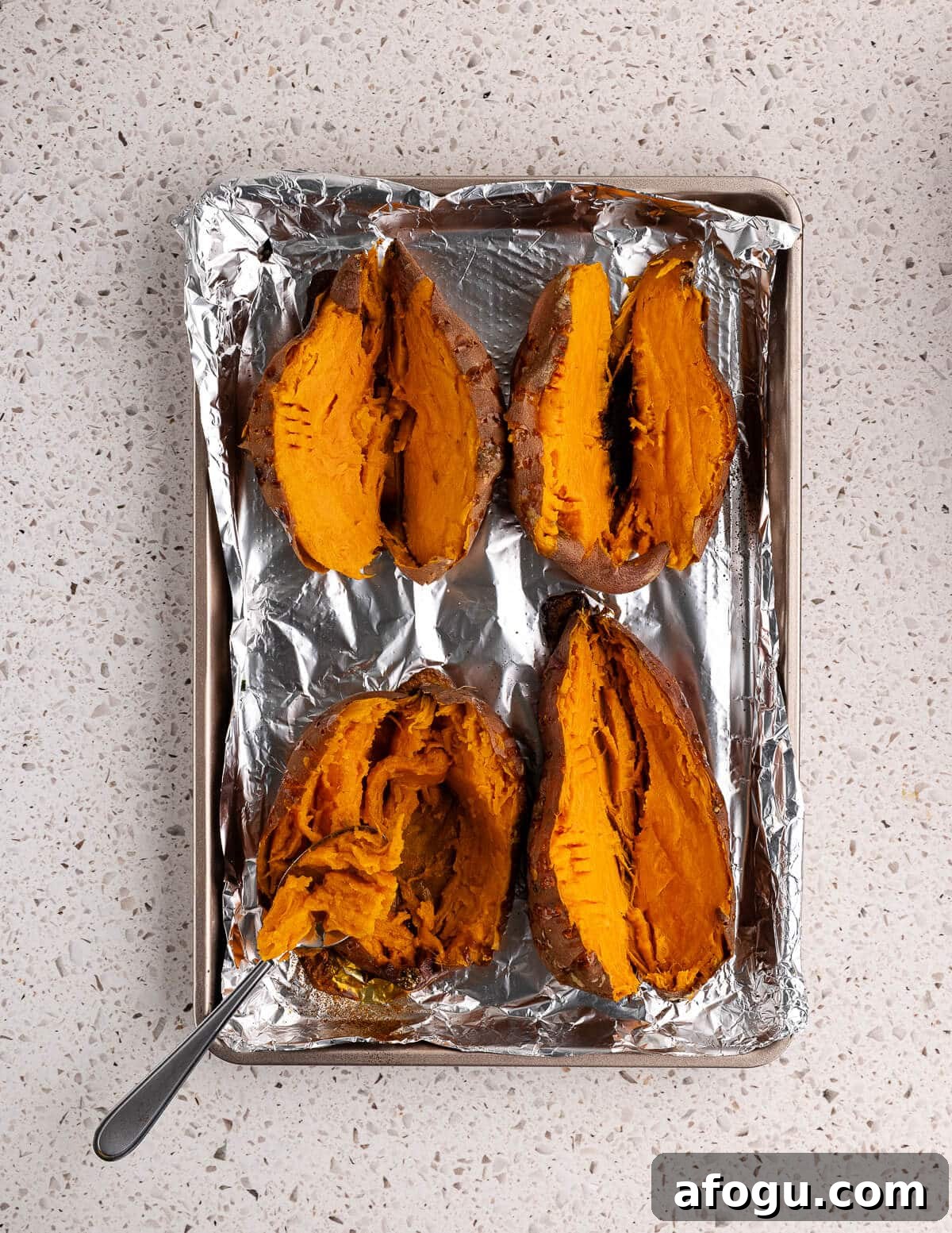 baked sweet potatoes cut in half on a sheet pan. 