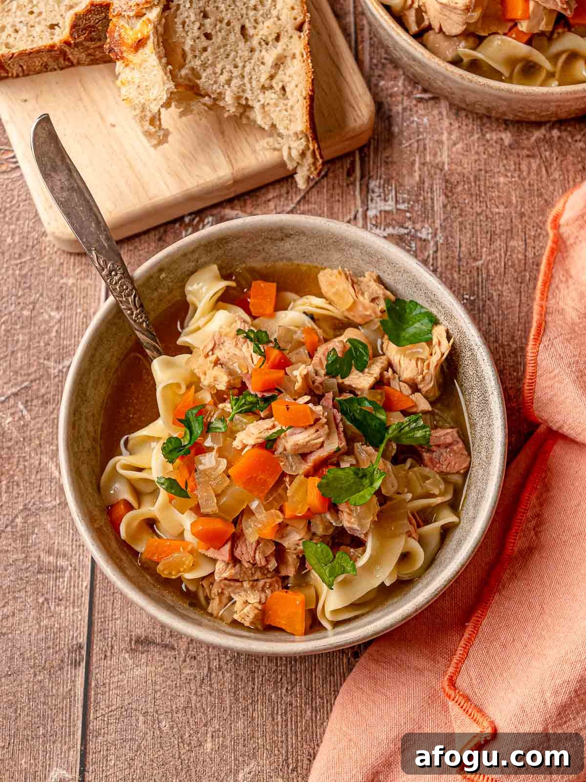 Bowl of turkey noodle soup with noodles, vegetables, and bread on the side.