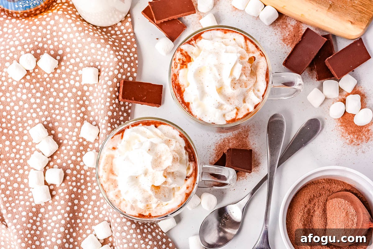 Overhead collage of copycat Swig Nutcracker hazelnut hot chocolate topped with whipped cream, surrounded by cocoa mix, marshmallows, and labeled ingredients for an easy homemade hot cocoa recipe.