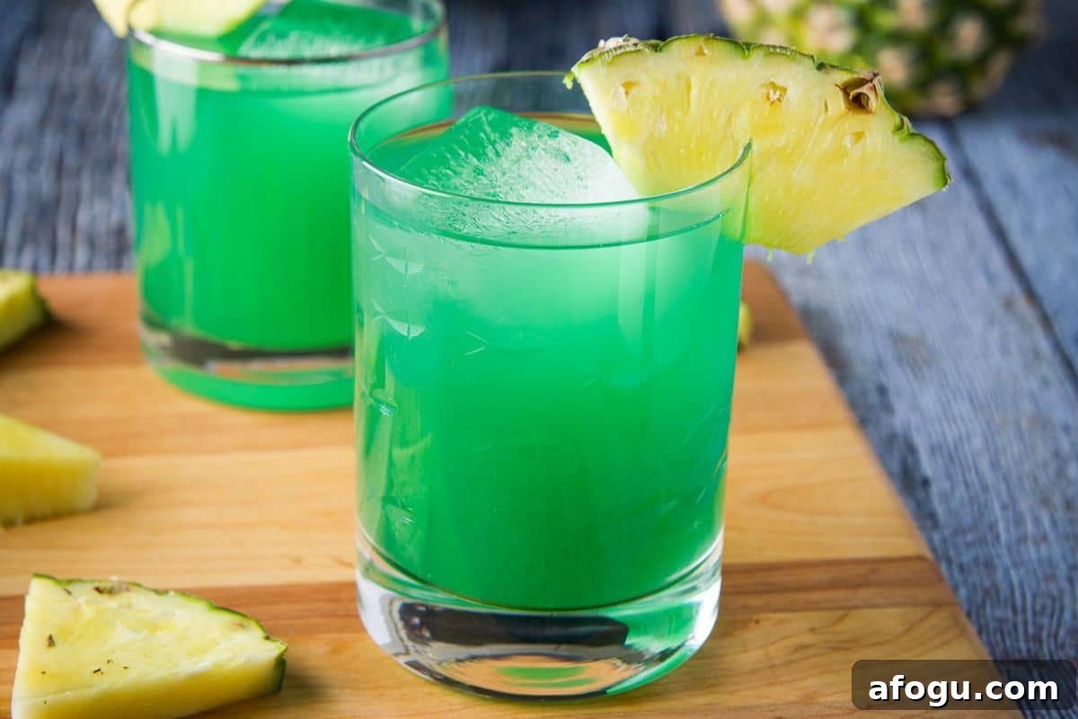 close up of two green cocktails on a board with pineapple as garnish