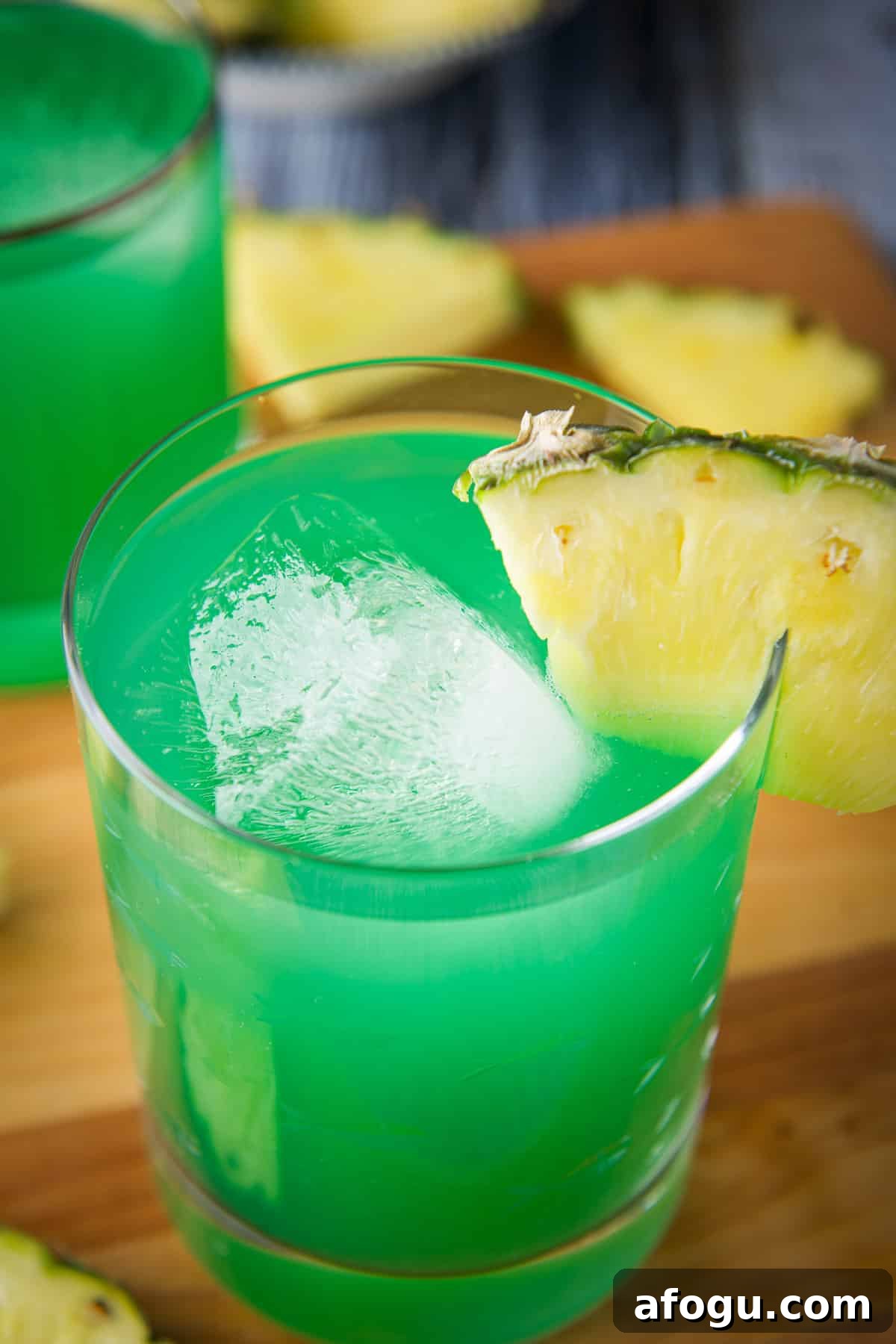 Close up of a glass of drunk leprechaun with a pineapple wedge on the rim. There is also another drink in the back with pineapple wedges