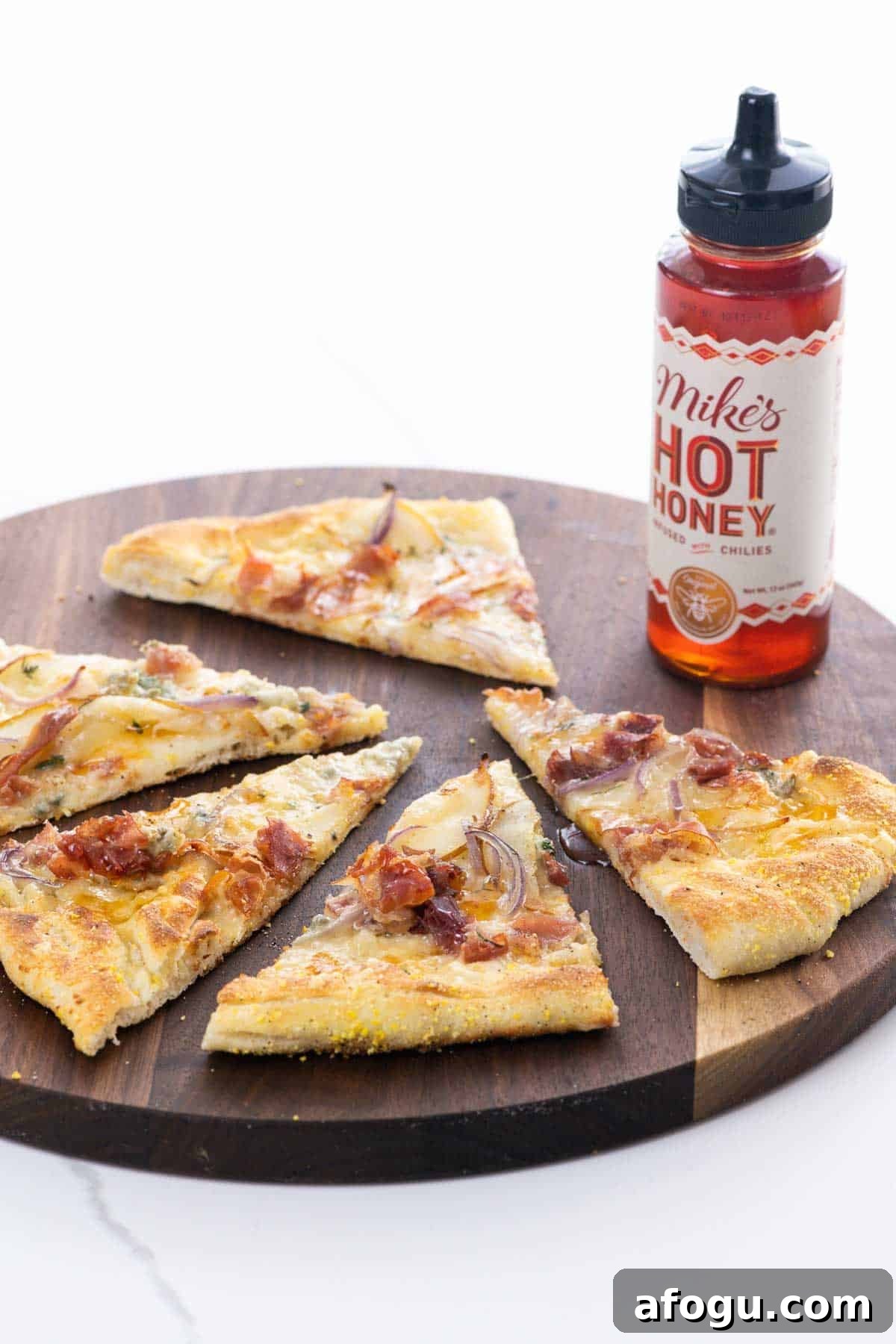 Pear and Gorgonzola Pizza Recipe with Honey and Walnuts 2 pear gorgonzola pizza with prosciutto and hot honey on a cutting board with a bottle of hot honey