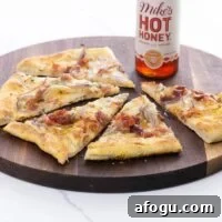 Pear and Gorgonzola Pizza Recipe with Honey and Walnuts 6 pear gorgonzola pizza with prosciutto and hot honey on a cutting board with a bottle of hot honey