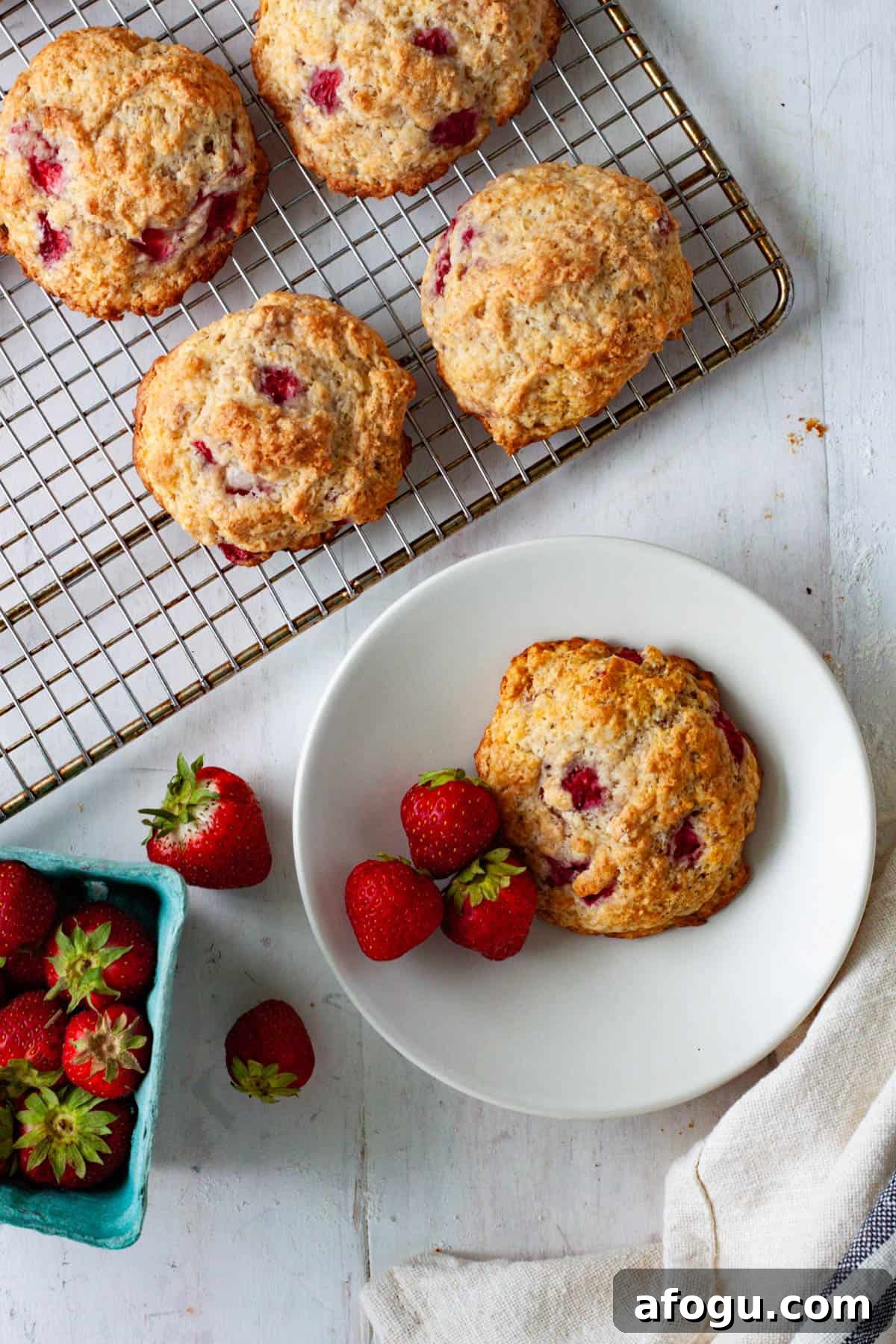 A strawberry biscuit on a small plate with more strawberry biscuits on a cooling rack.
