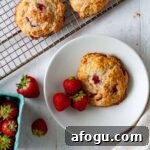 A strawberry biscuit on a small plate with more strawberry biscuits on a cooling rack.