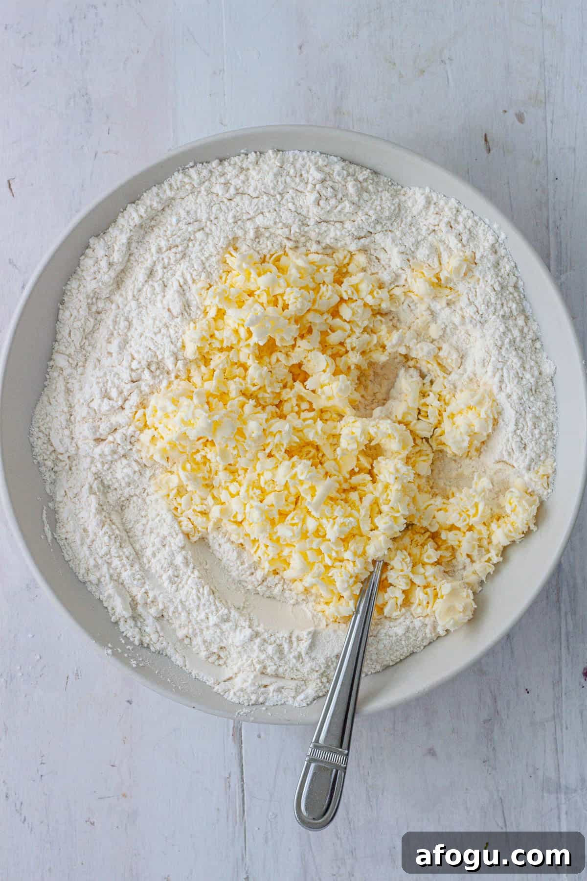 Grated butter in a bowl with the dry ingredients for drop biscuits.