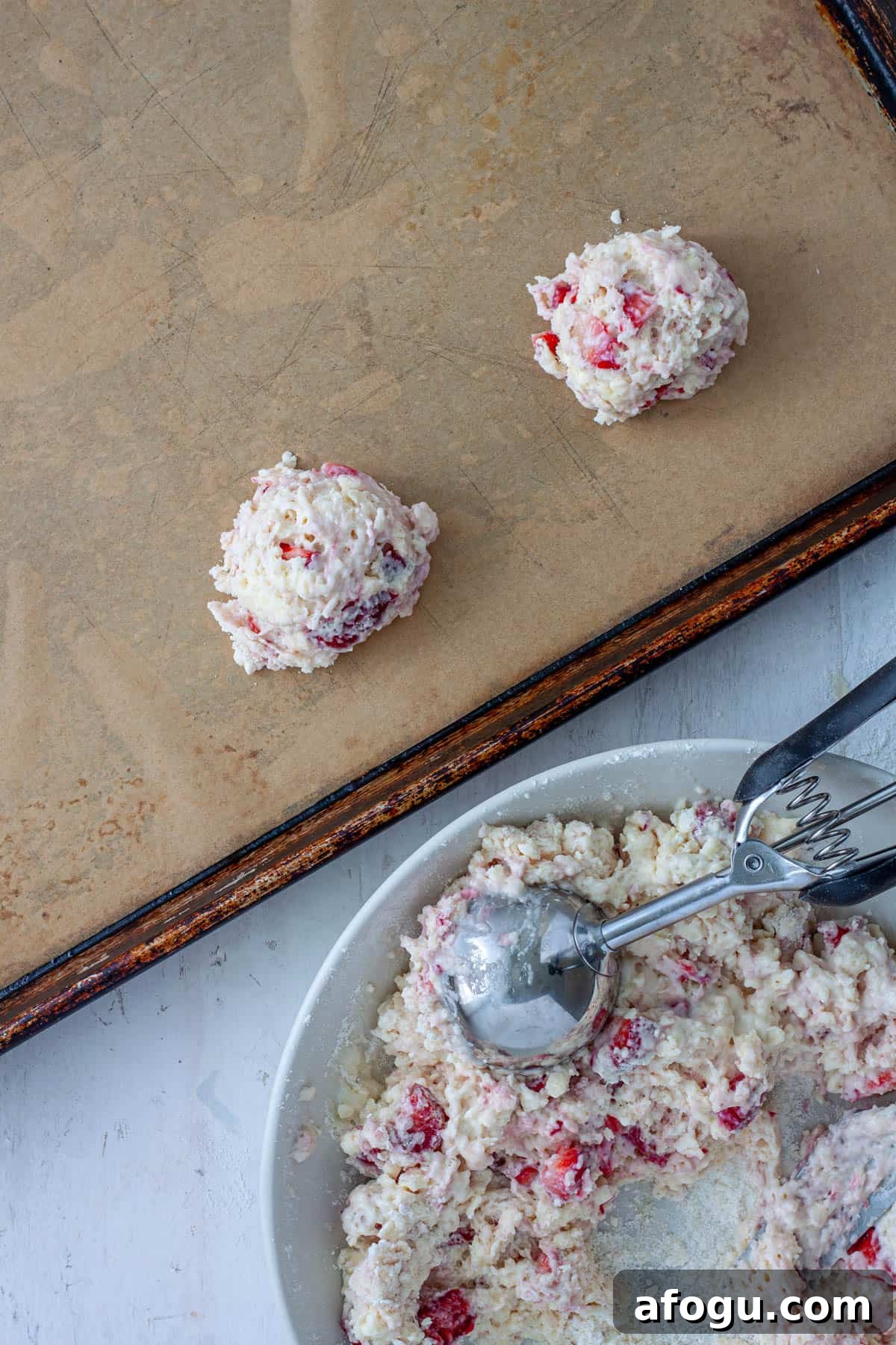 Strawberry biscuits getting scooped and placed on a parchment lined baking sheet.