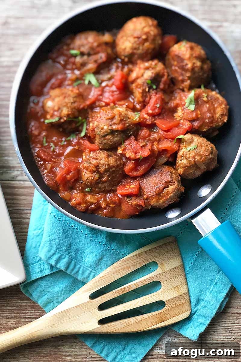 Spanish Nochebuena Christmas Dinner Menu and Traditions 2 Vertical image of a pan filled with meatballs and stewed tomatoes on a blue napkin next to a wooden spoon.