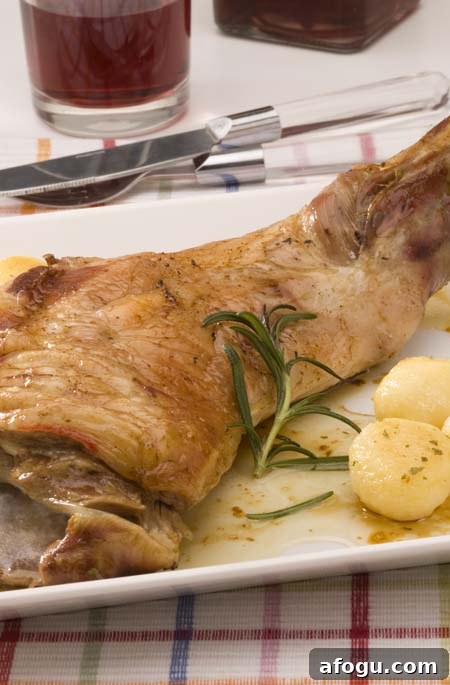 Spanish Nochebuena Christmas Dinner Menu and Traditions 4 Roasted Rosemary Lamb with Potatoes, with a sprig of rosemary on a white serving platter.