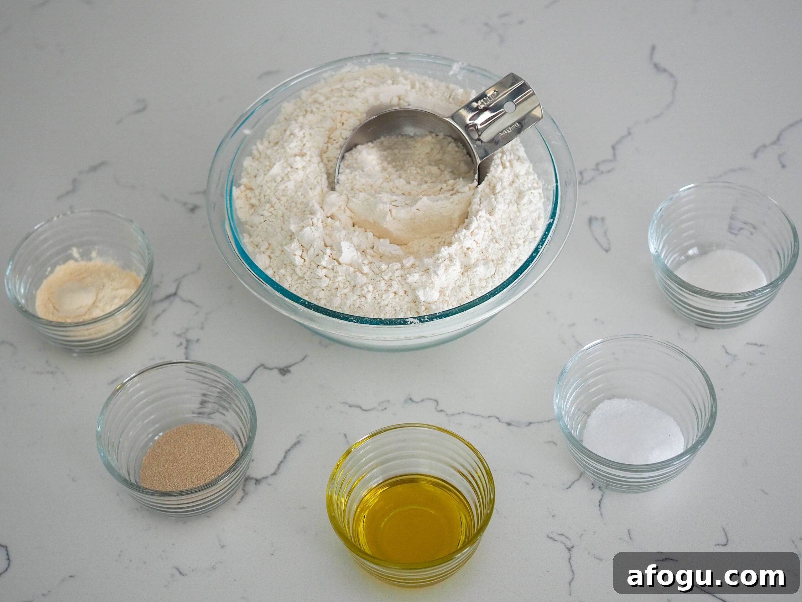 A bowl of flour with a measuring cup sticking out of it, along with small filled ingredient bowls surrounding it.