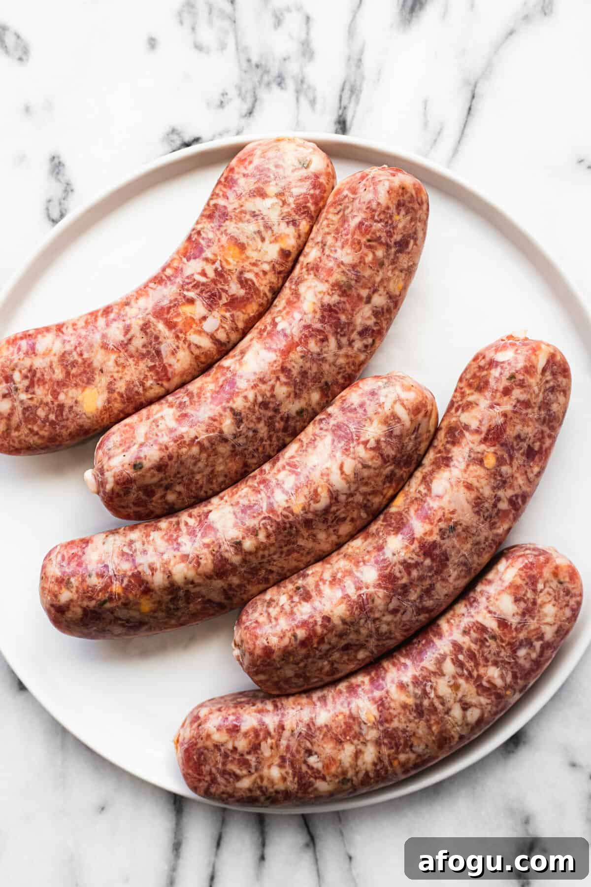 Raw cheddar jalapeno bratwurst on a white plate.