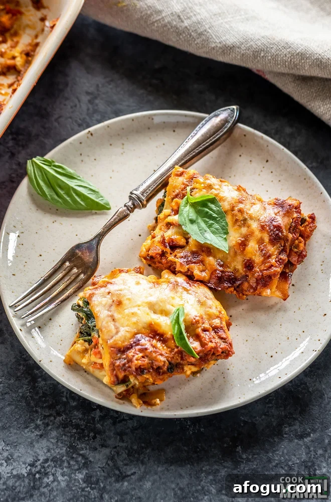 two slices of vegetable paneer lasagna served in a white plate with a fork placed on the side