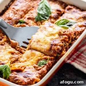 paneer lasagna in an orange color baking dish with a spatula scooping out a portion from the lasagna
