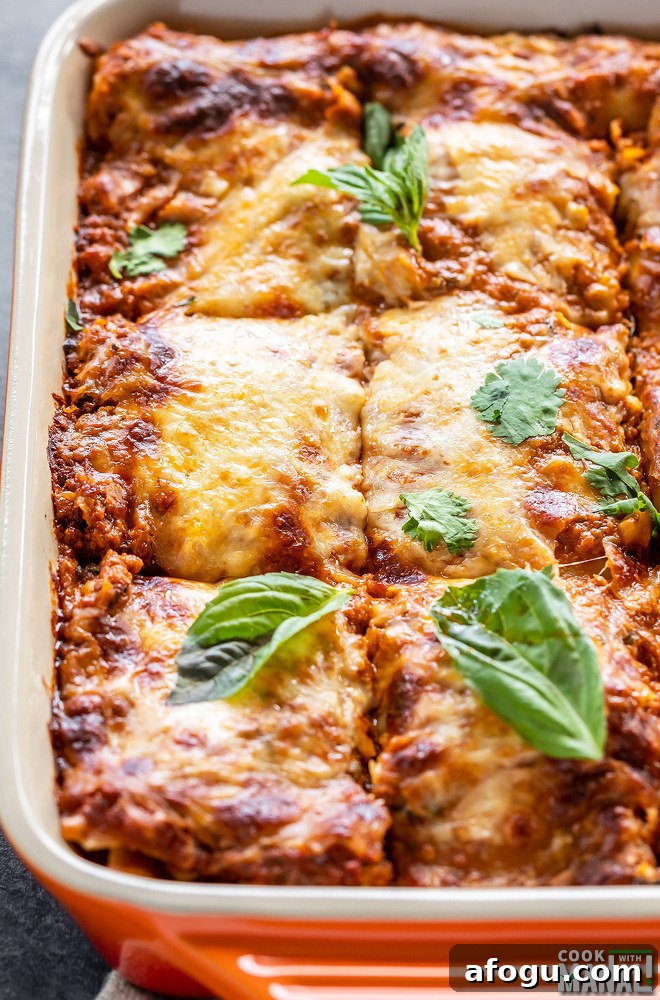 vegetable paneer lasagna in an orange baking dish topped with basil and cilantro