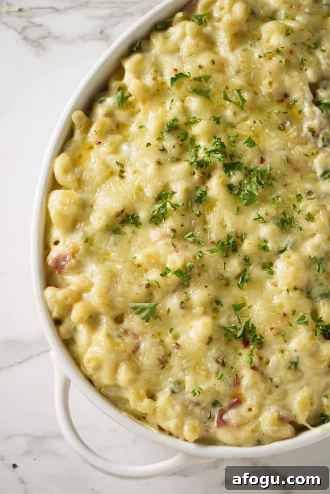 macaroni and cheese in a white ceramic baking dish topped with melted pepper jack cheese with chunks of bacon and topped with green garnish on top of a marble surface