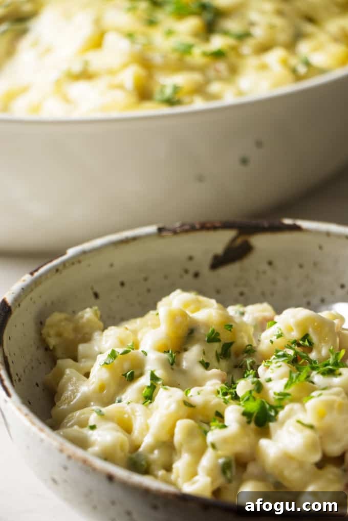 macaroni and cheese in a stone bowl with a spoon and topped with a green garnish. White baking dish in background filled with mac and cheese