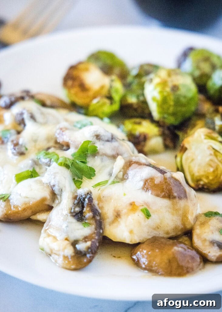 chicken with mushrooms and cheese on a white plate with brussel sprouts