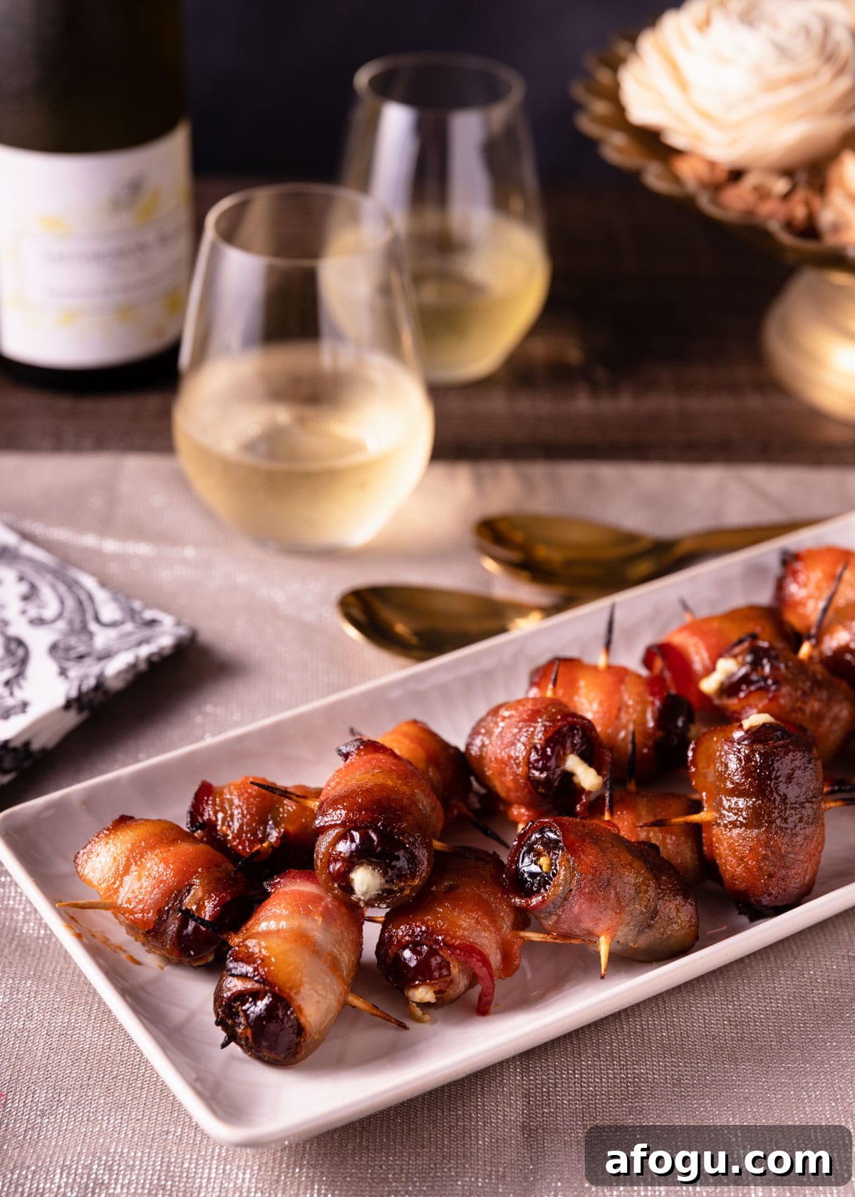 maple sriracha devils on horseback on a white serving platter surrounded by napkins and glasses of wine