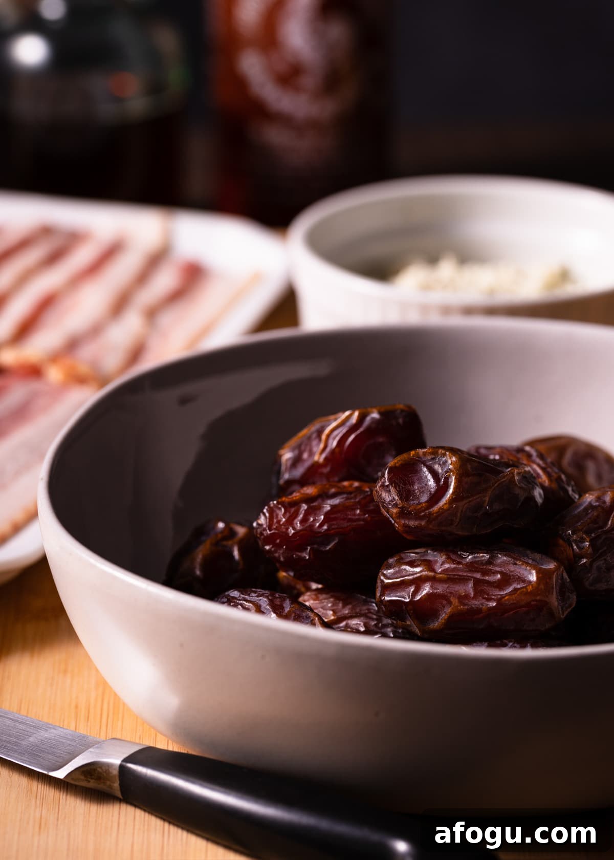 a bowl of medjool dates with a bowl of crumbled blue cheese and a platter of raw bacon in the background