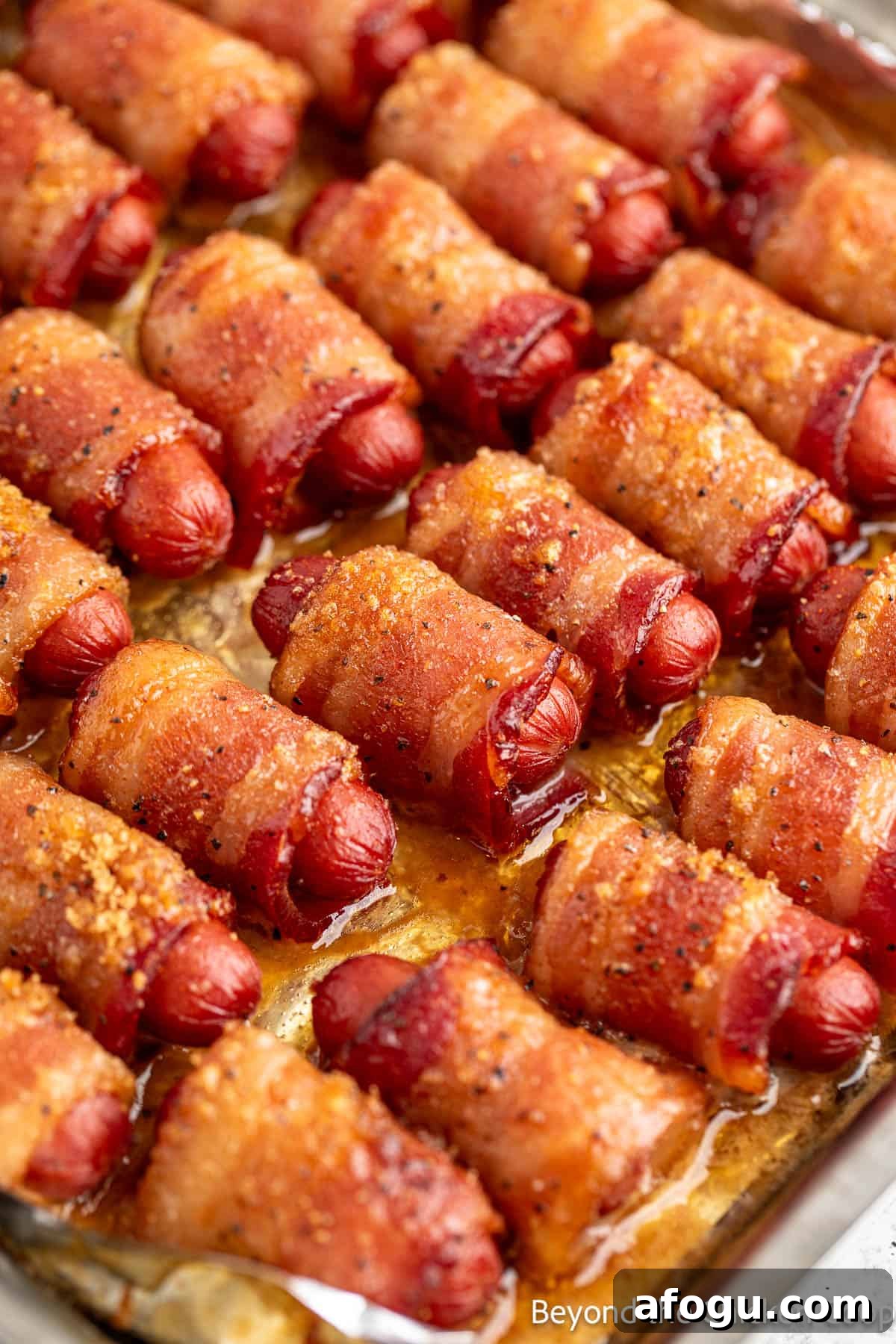 Baked little smokies wrapped with bacon on a baking sheet.