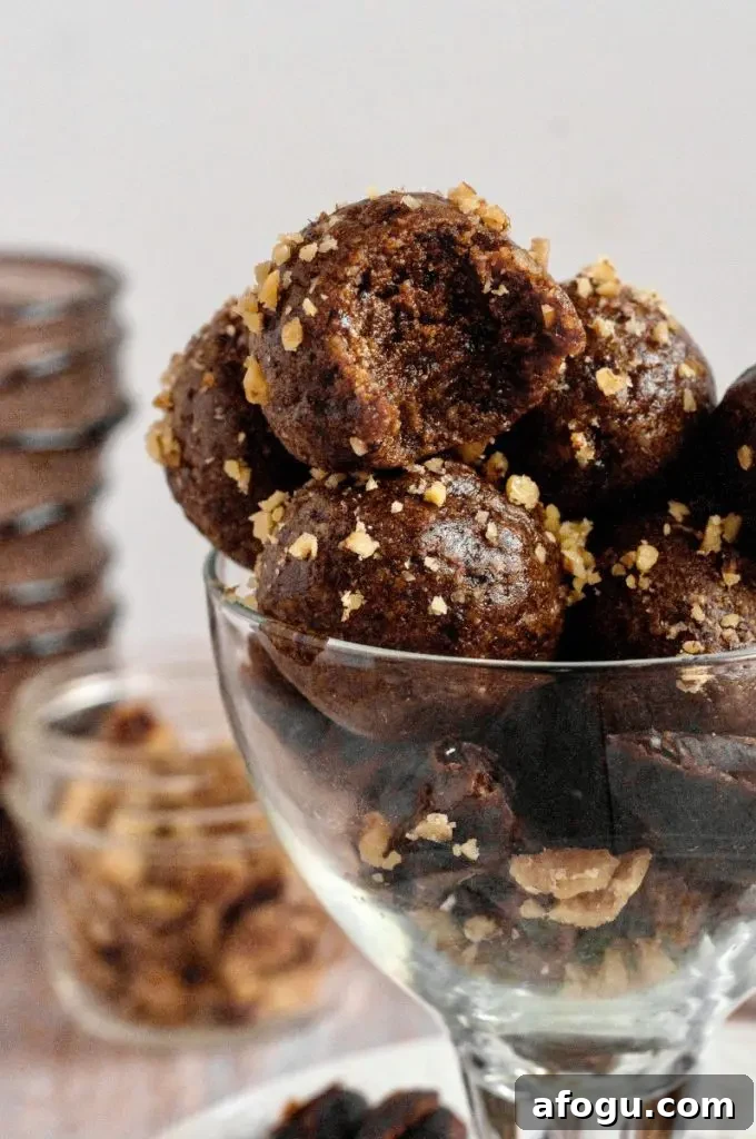 Dark brown pecan pie balls rolled in golden brown pecan crumbs and placed in a glass cup.