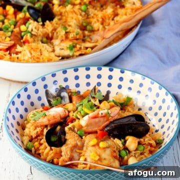 Authentic Spanish Paella Recipe: Traditional Seafood & Saffron Flavor 15 colorful rice with seafood on blue dotted plate with paella pan in background