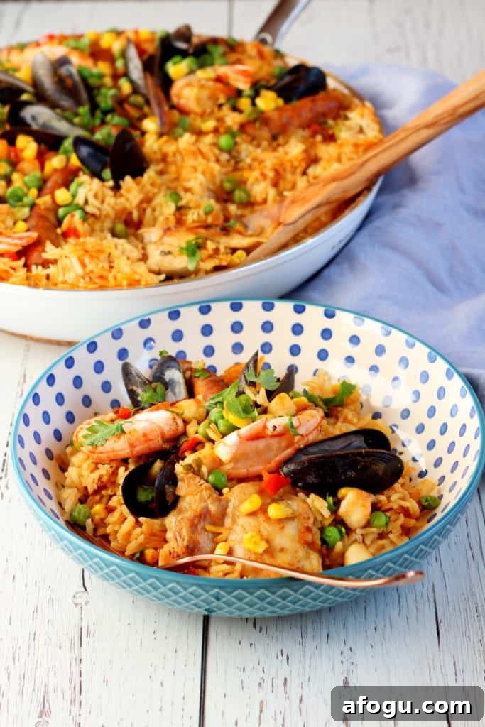 Authentic Spanish Paella Recipe: Traditional Seafood & Saffron Flavor 8 colorful rice with seafood on blue dotted plate with paella pan in background