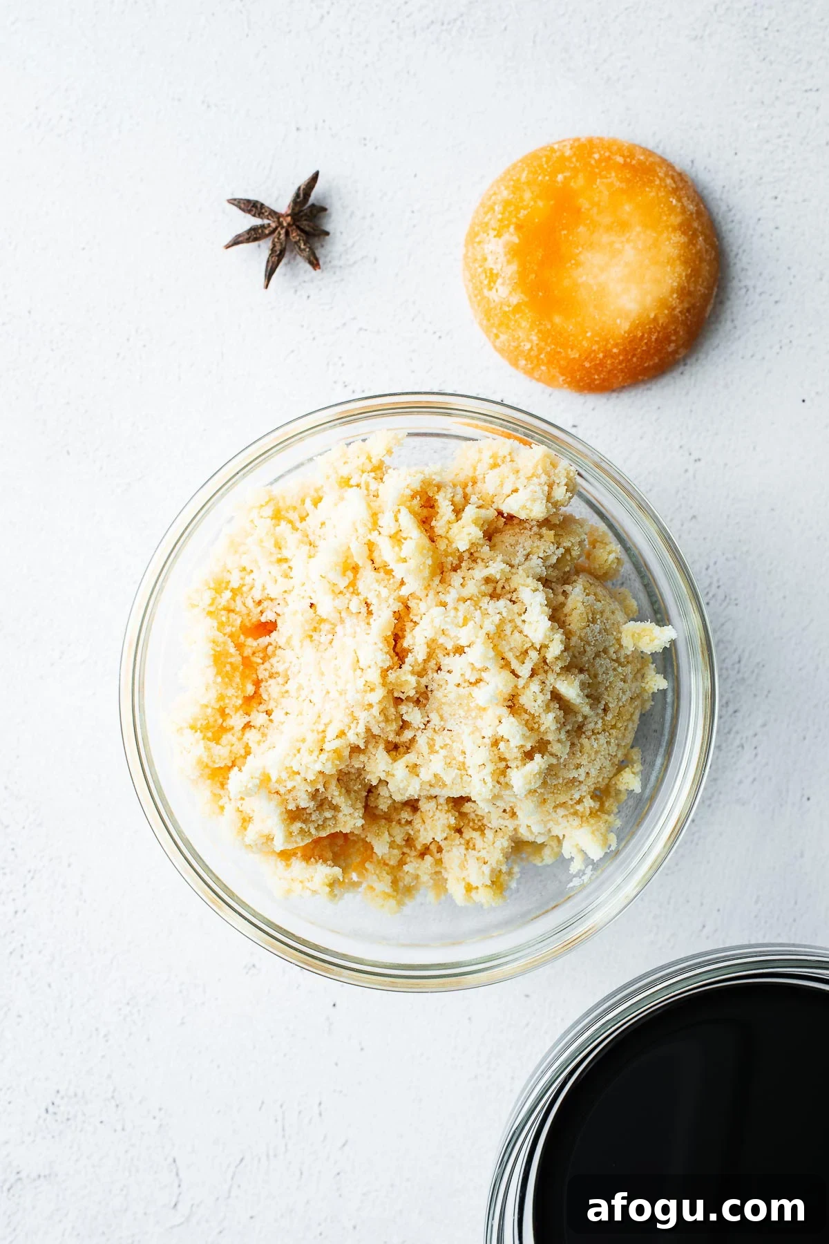 Sweet Soy Sauce Substitute: How to Replace Kecap Manis in Recipes 3 Ingredients for homemade sweet soy sauce (kecap manis) on a light concrete background, including a brick of palm sugar, a bowl of grated palm sugar, a star anise pod and a bowl of all-purpose soy sauce.