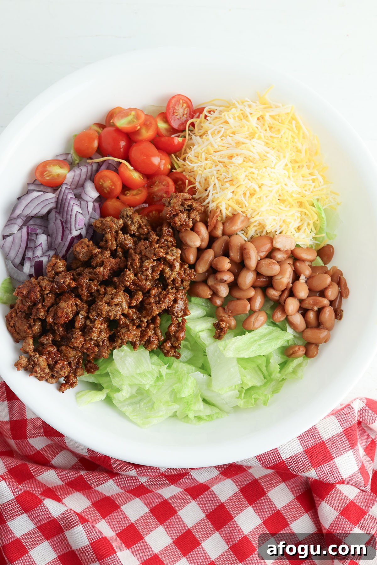 Lettuce, tomatoes, beans, red onion cheese, and taco meat in a bowl.
