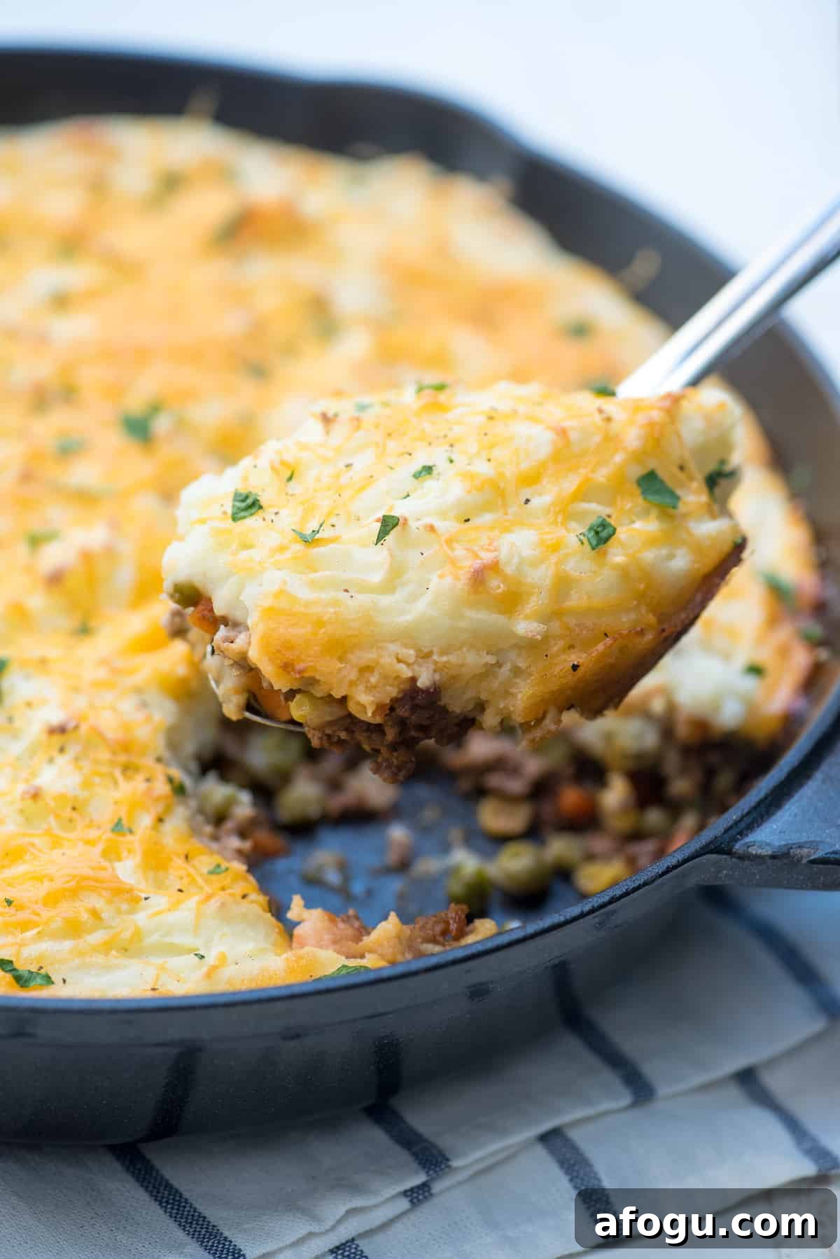 A spoon scooping shepherd's pie from a cast iron skillet.