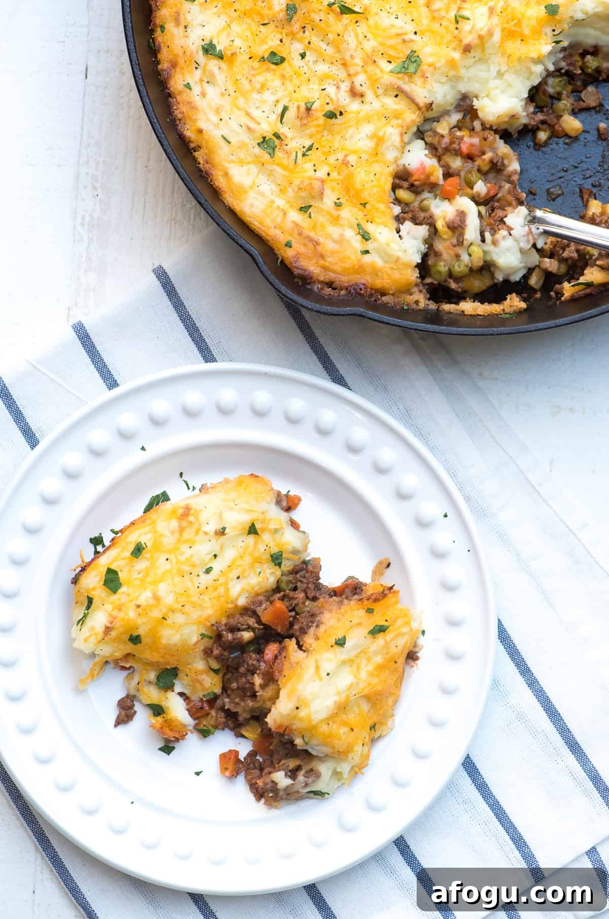 A serving of shepherd's pie on a white plate next to a cast iron skillet.