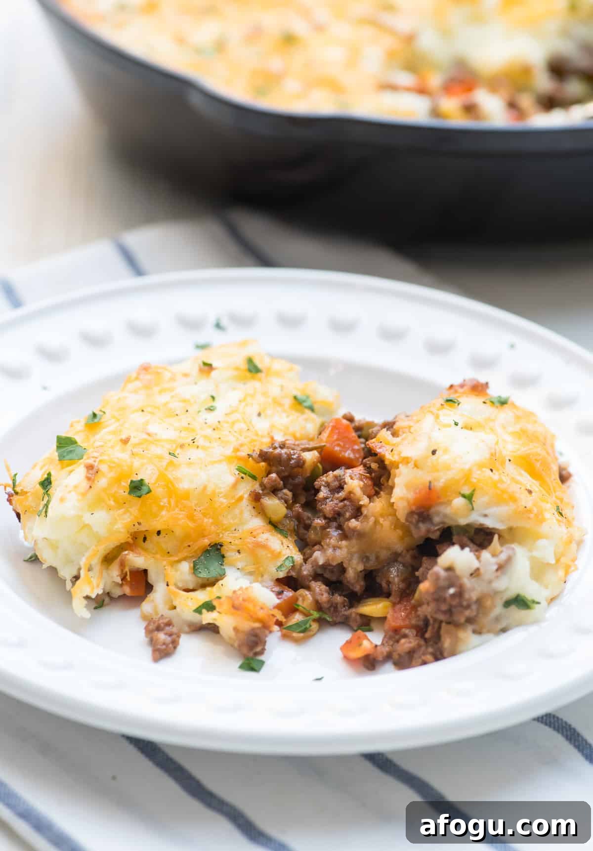 A serving of shepherd's pie with peas and carros on a white plate.