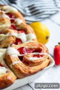 Close up of strawberry cinnamon roll in a large white baking dish on a white counter.