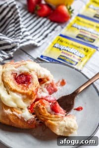 Strawberry roll on a gray plate with gold fork cutting into it.