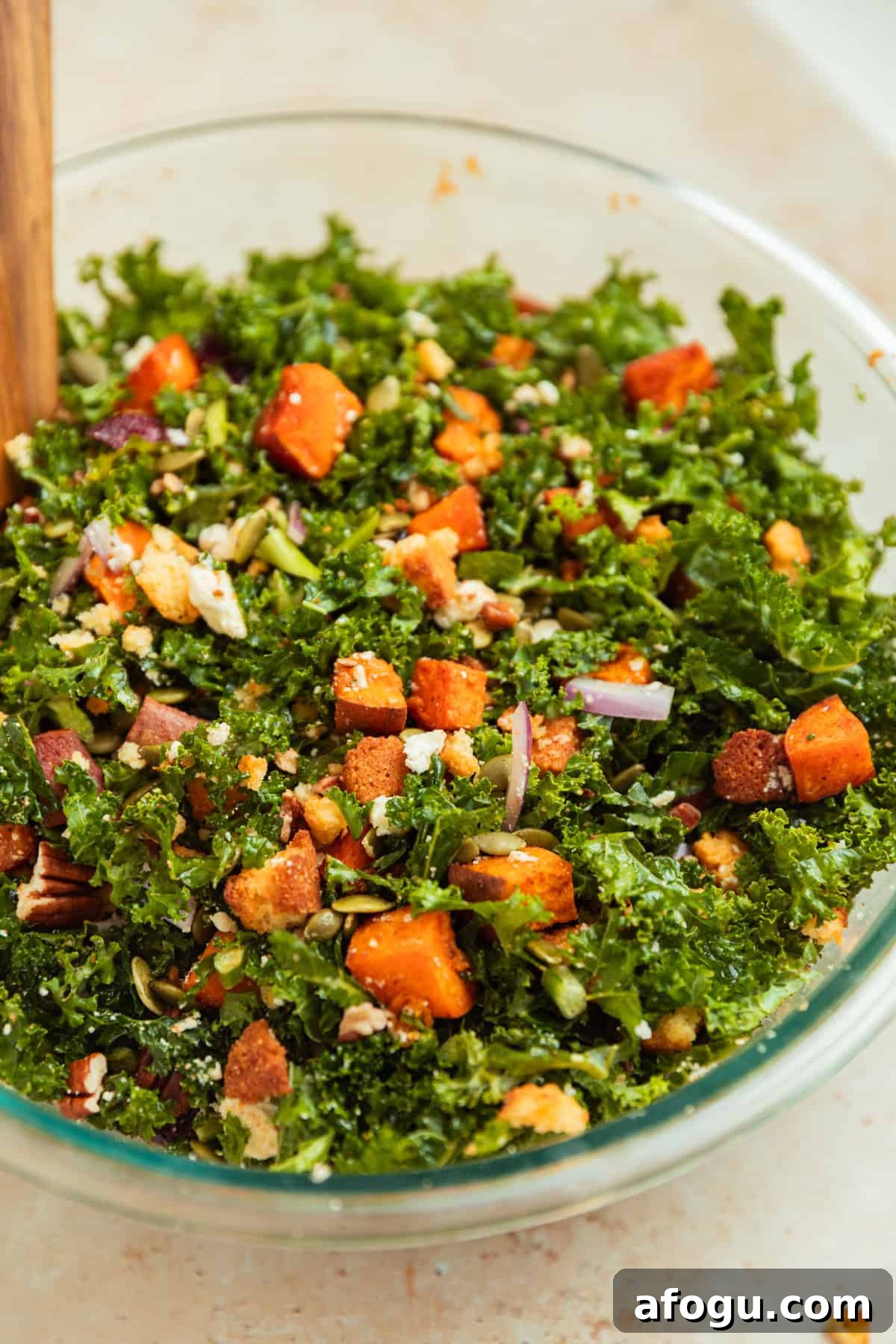Tossed sweet potato kale salad in glass bowl with tongs.