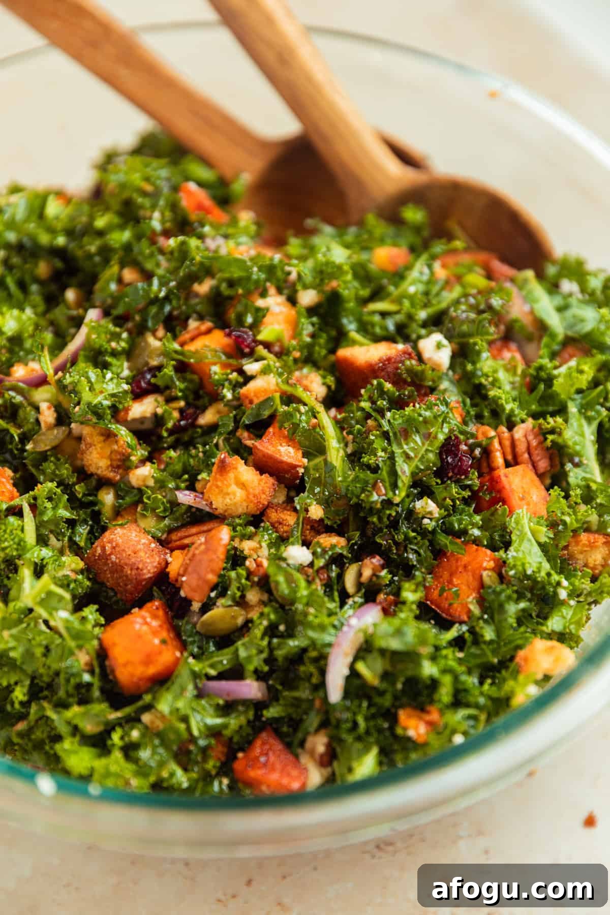 Dressing added to kale salad and tossed in with wood spoons.