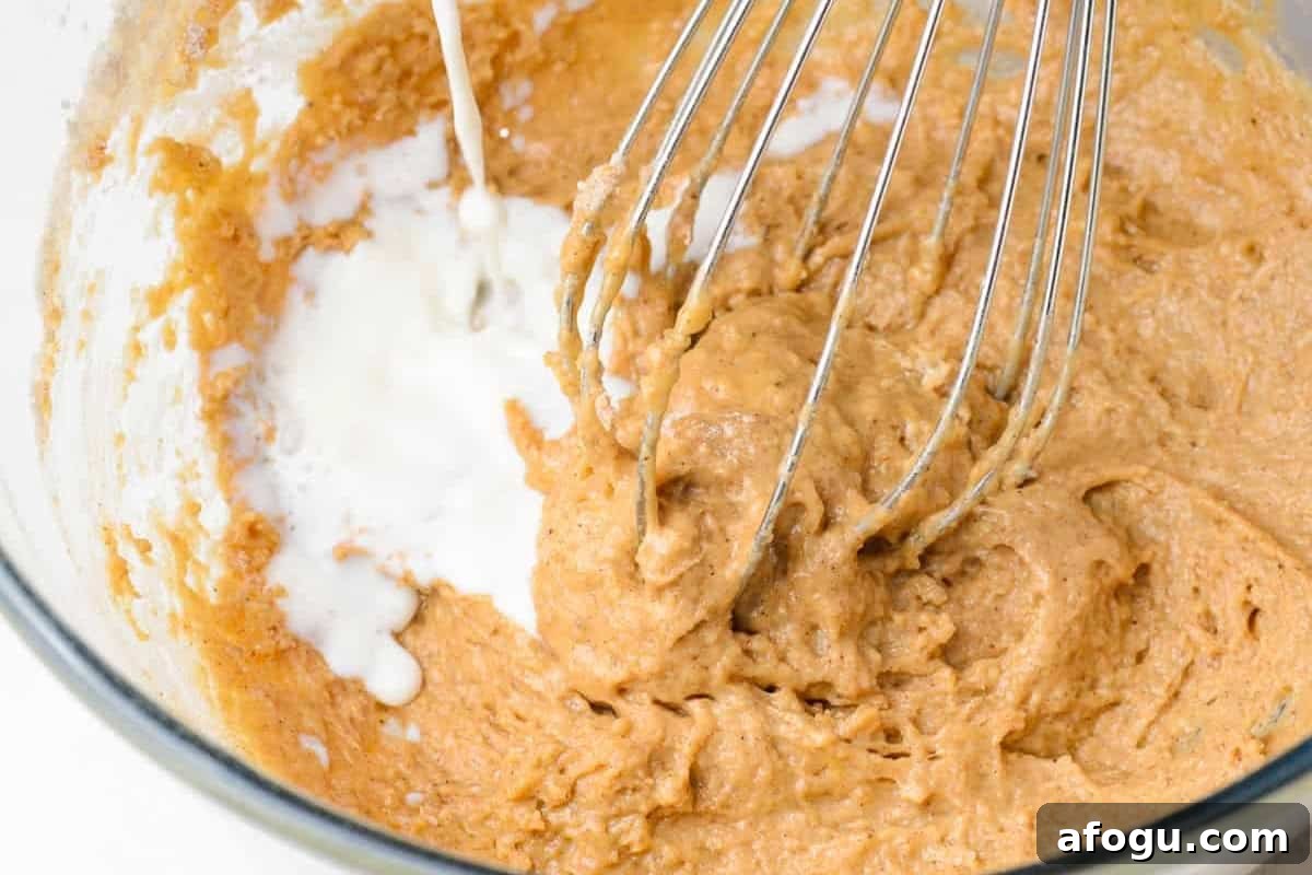 adding milk to batter in a glass bowl with a whisk.